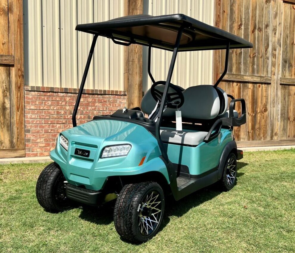 A teal golf cart parked on grass with a black roof and stylish wheels.