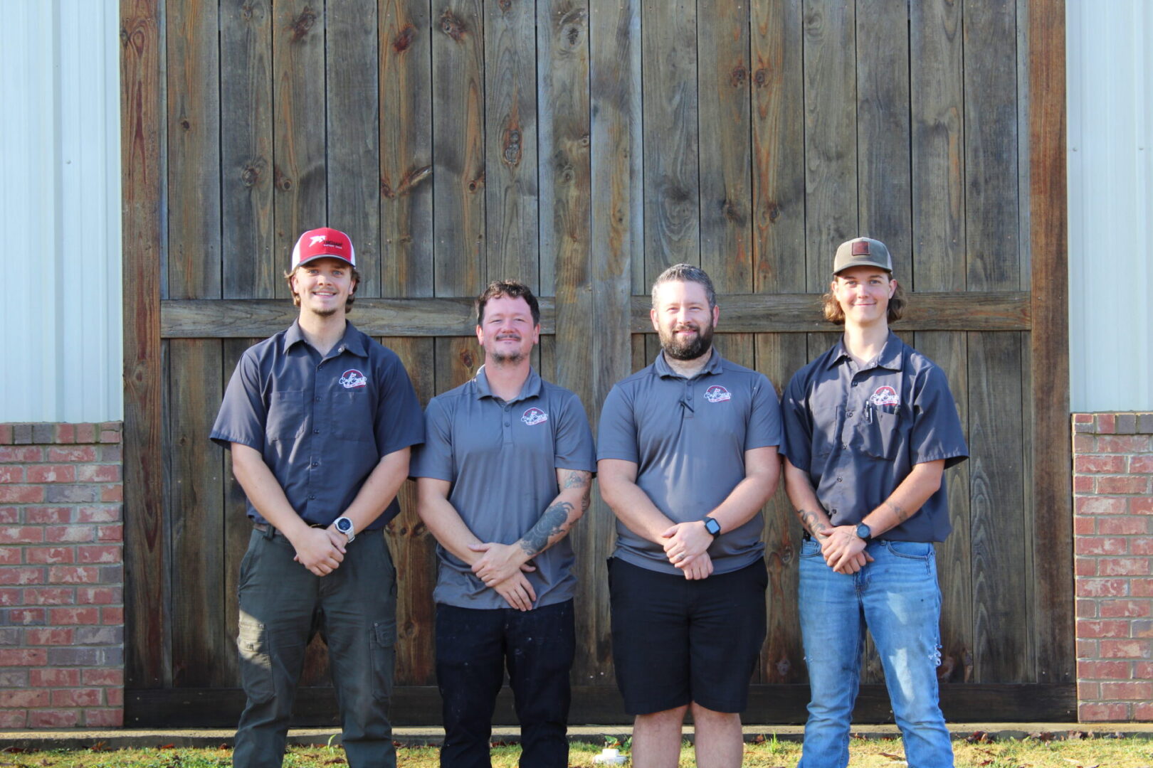 Four men standing in front of a wooden wall, casually dressed.