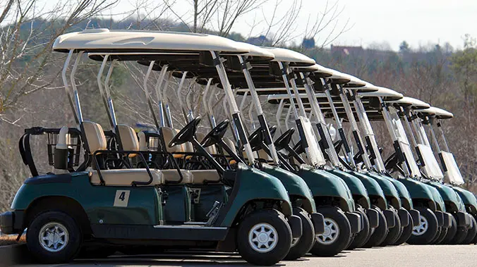A row of golf carts parked in a parking lot.