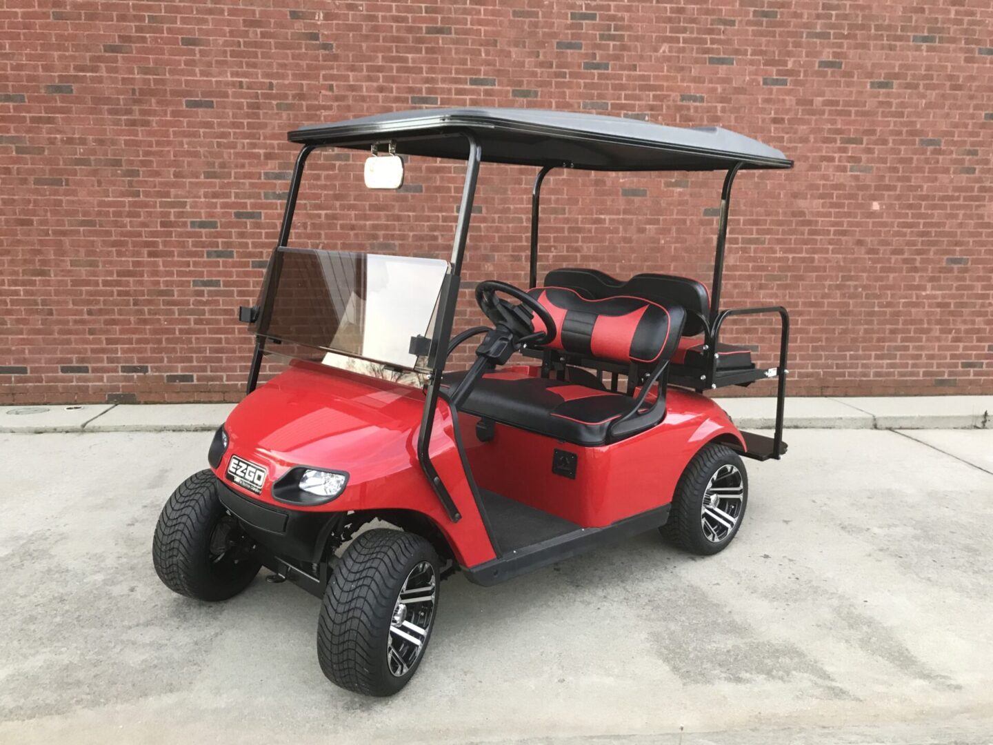 A red golf cart parked in front of a brick wall.