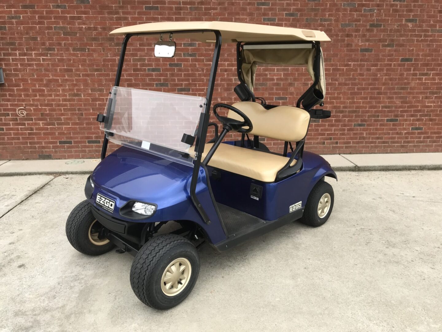 A blue golf cart with tan seats parked in front of a brick wall.