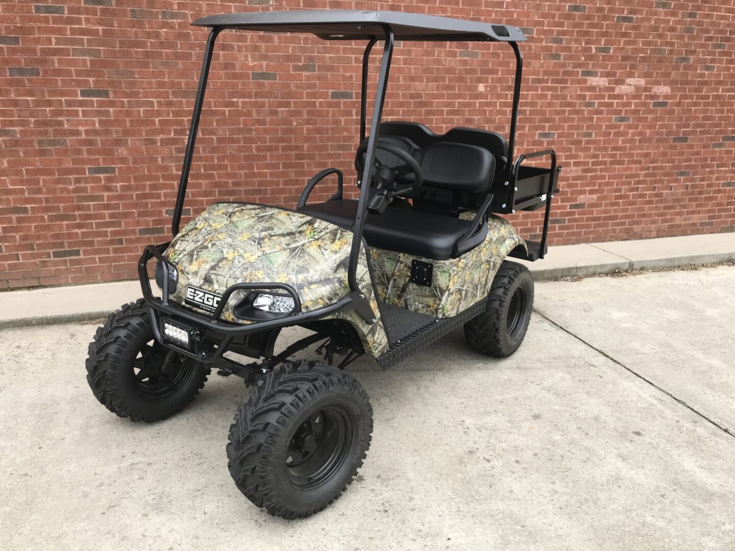 A golf cart with camouflage paint parked in front of a brick wall.