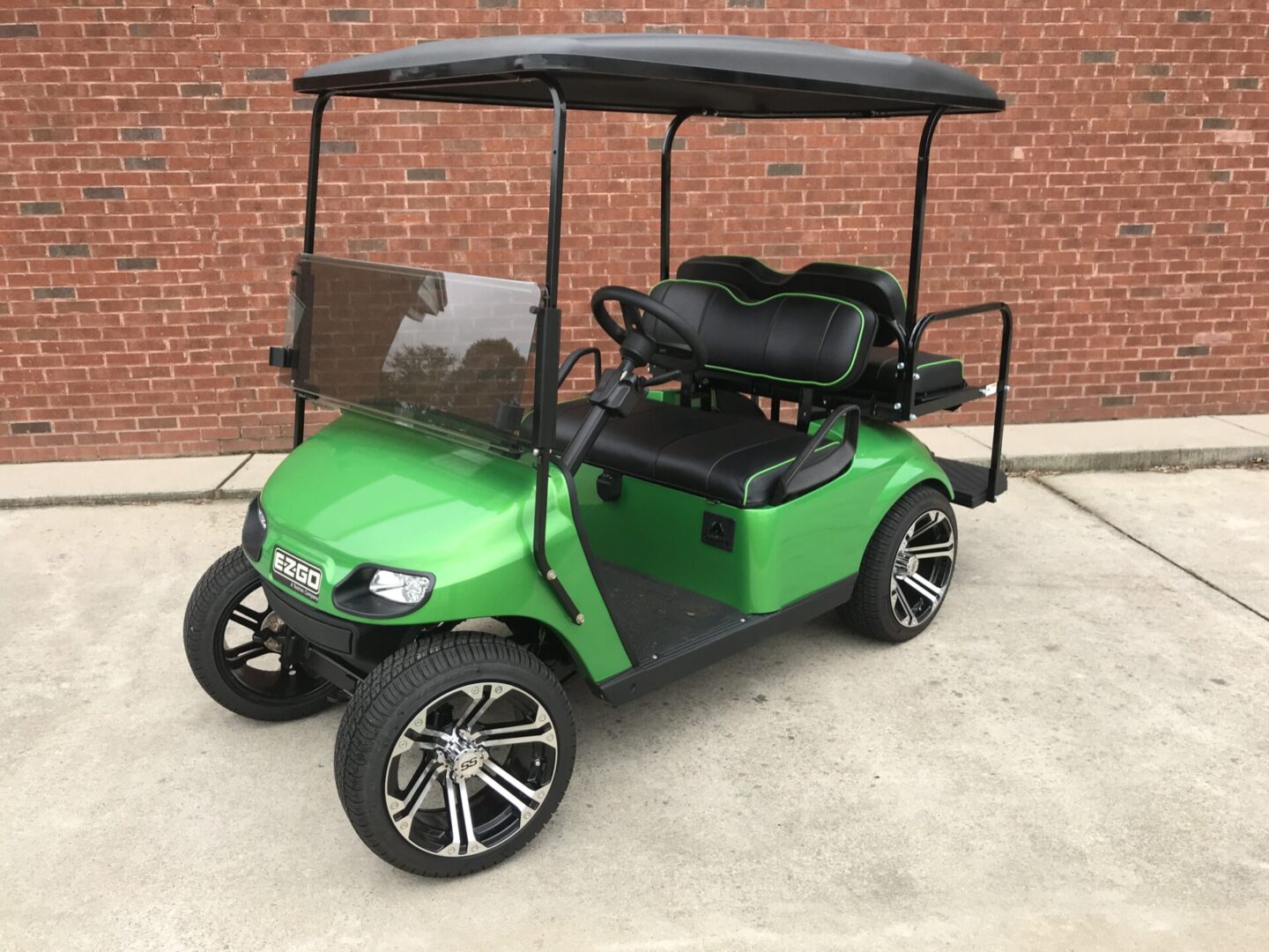 A green golf cart with black wheels parked in front of a brick wall.