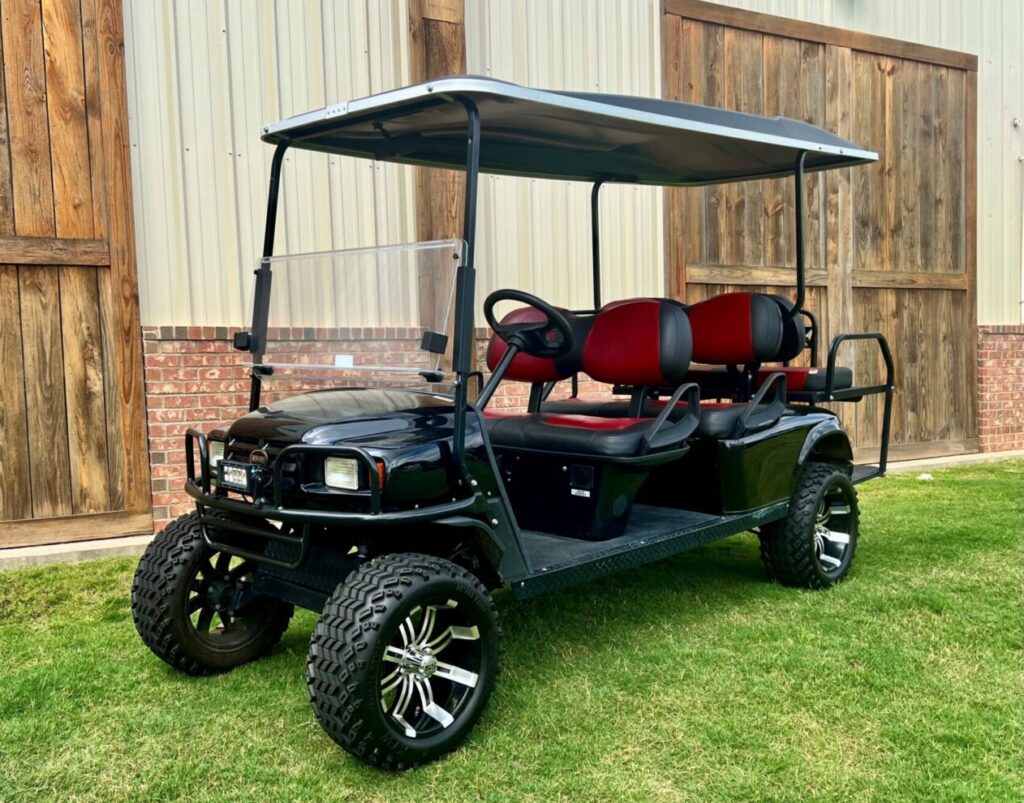 Black six-seater golf cart with red seats parked on grass.