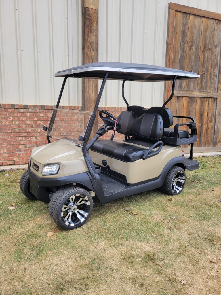 Beige golf cart parked on grass near a brick building.