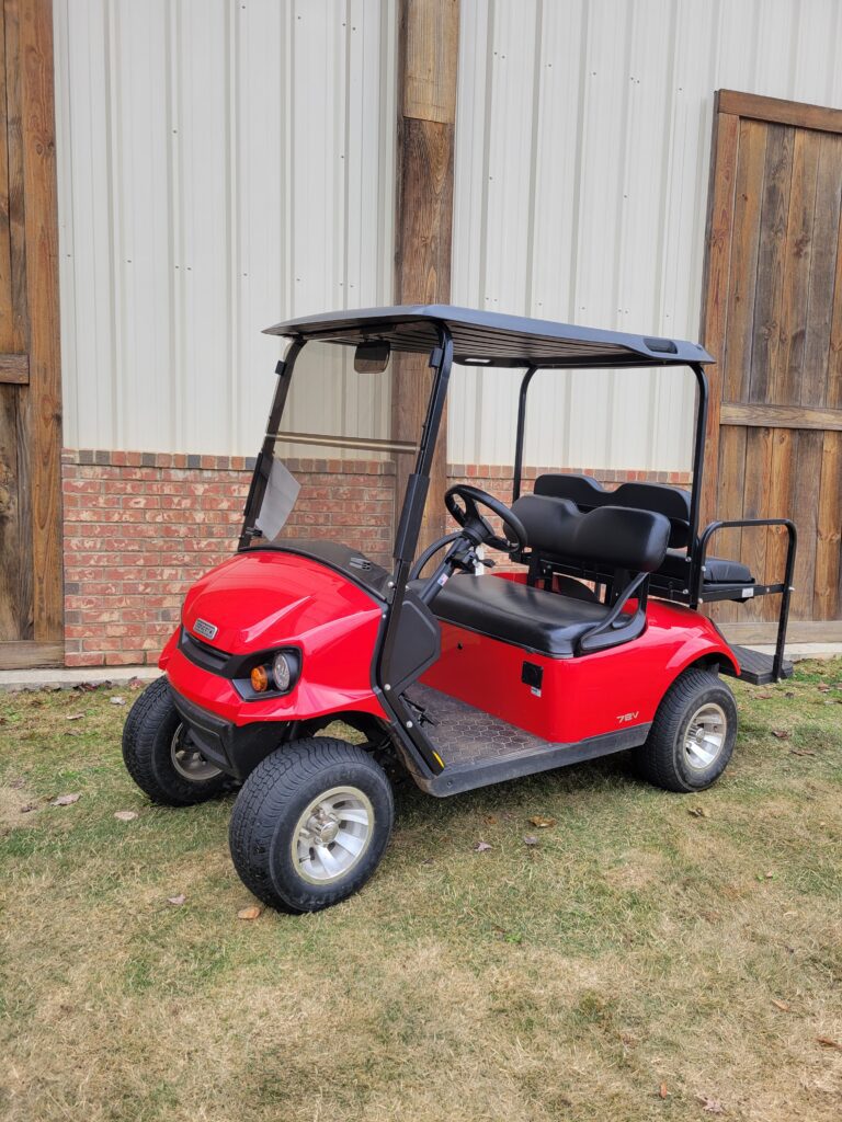 Red golf cart parked on grass near a wooden fence.