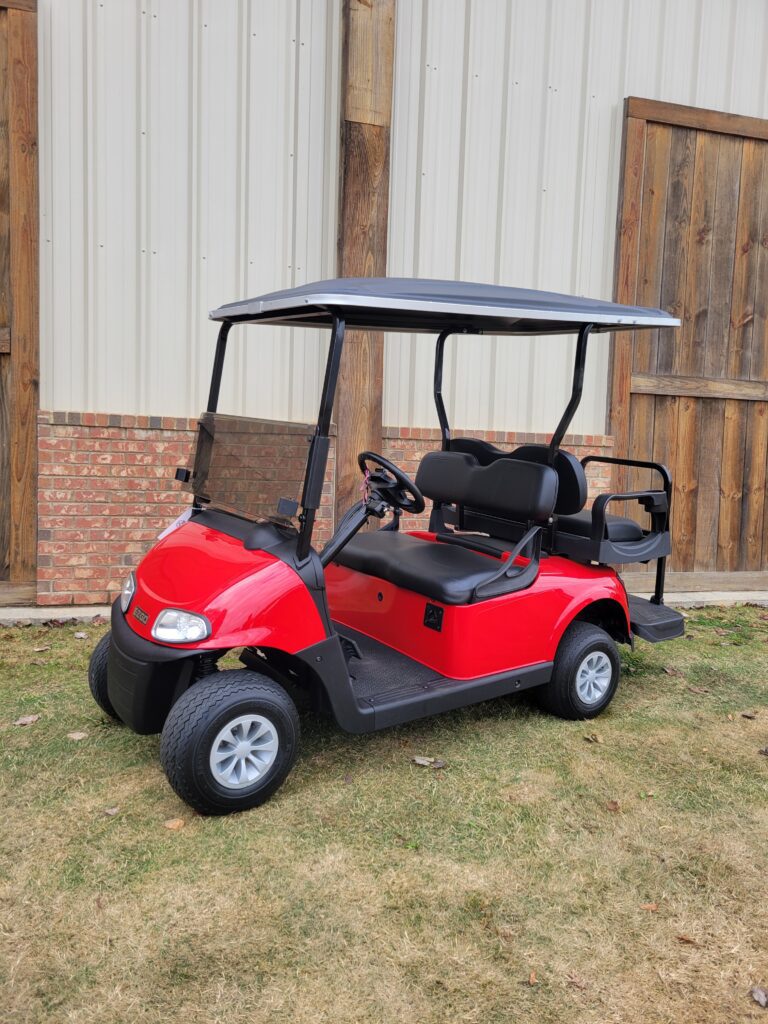 Red golf cart parked on grass near a building.