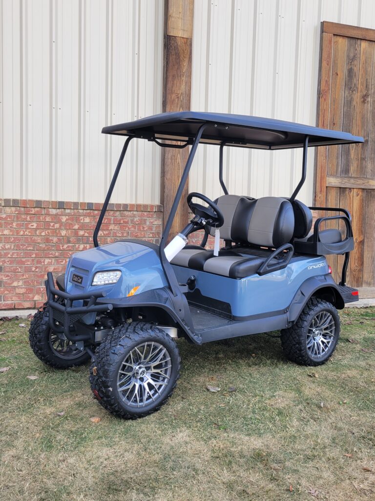 Blue golf cart with lifted suspension and custom wheels parked on grass.