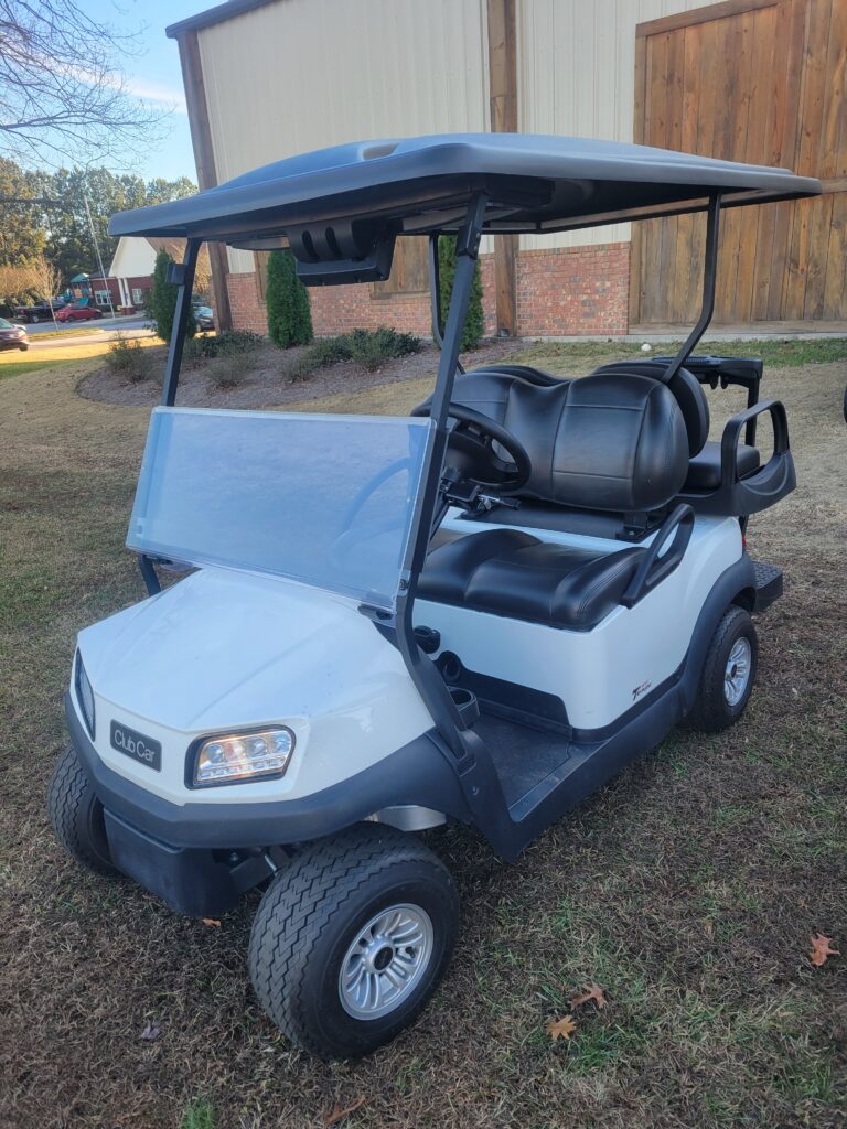 A white golf cart parked on grass with a roof and black seats.