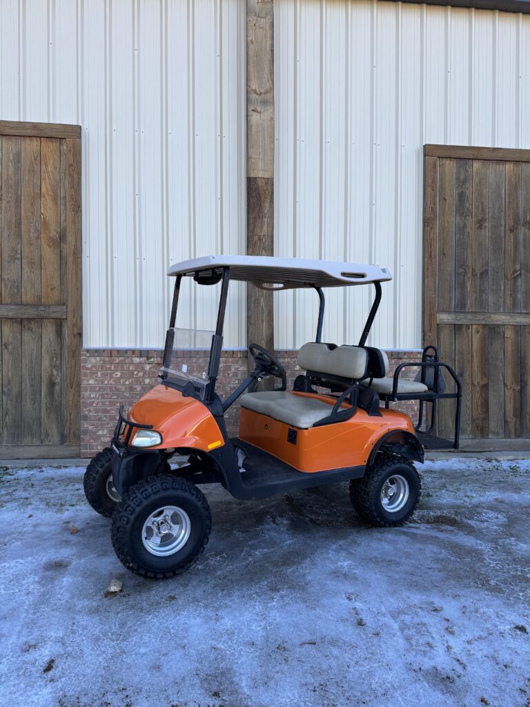 Orange golf cart parked outside near wooden doors.