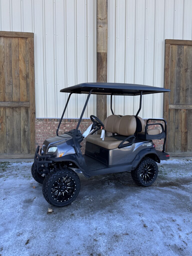 A sleek black golf cart parked outside wooden doors on a snowy surface.