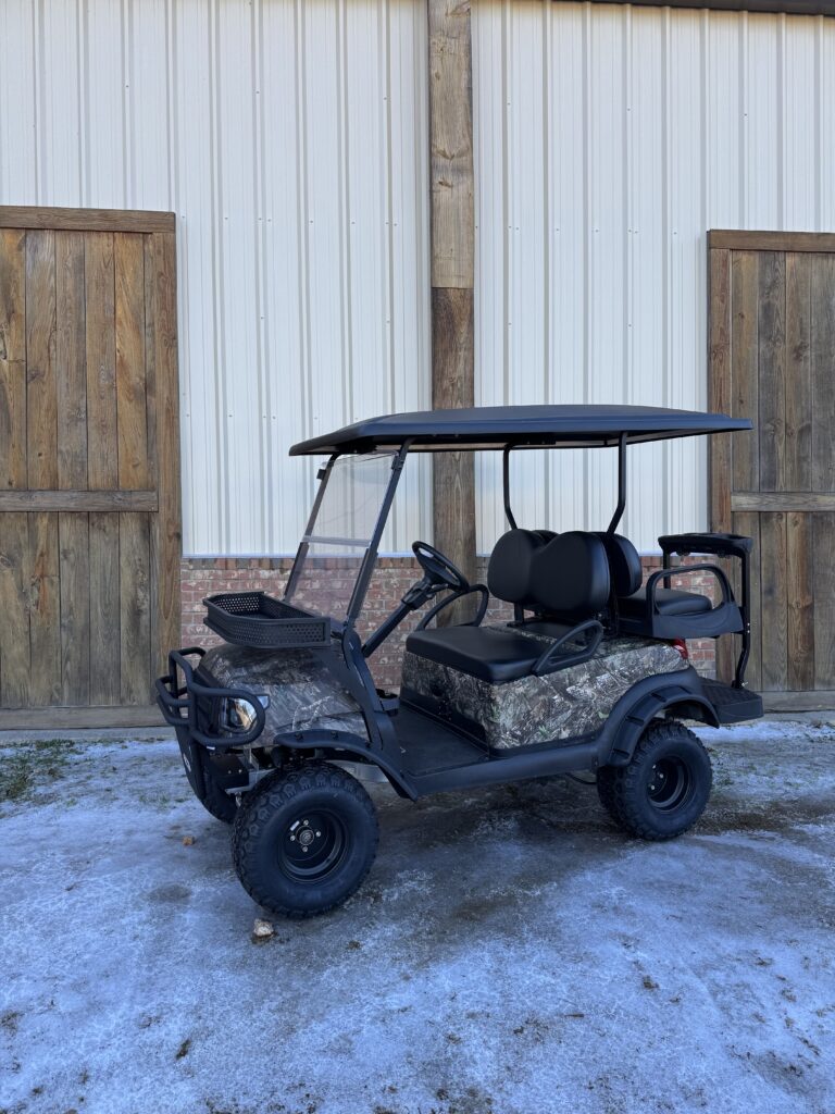 Camouflaged golf cart parked outside a building with wooden doors.