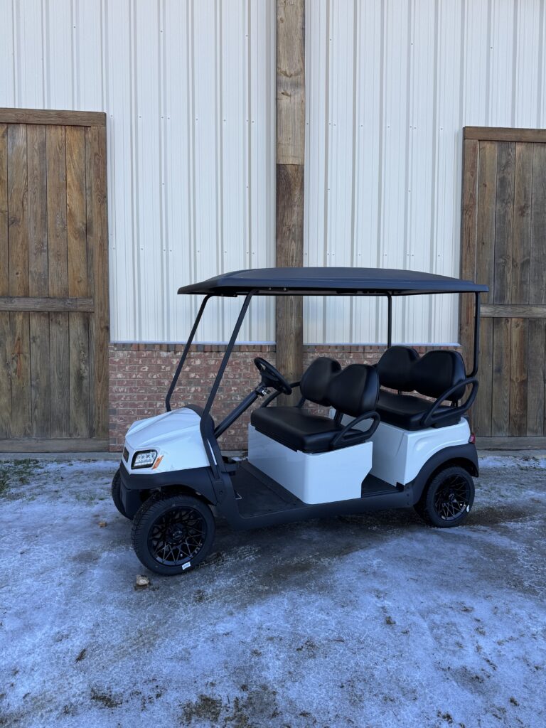 White golf cart with black roof and seats parked outside wooden doors.