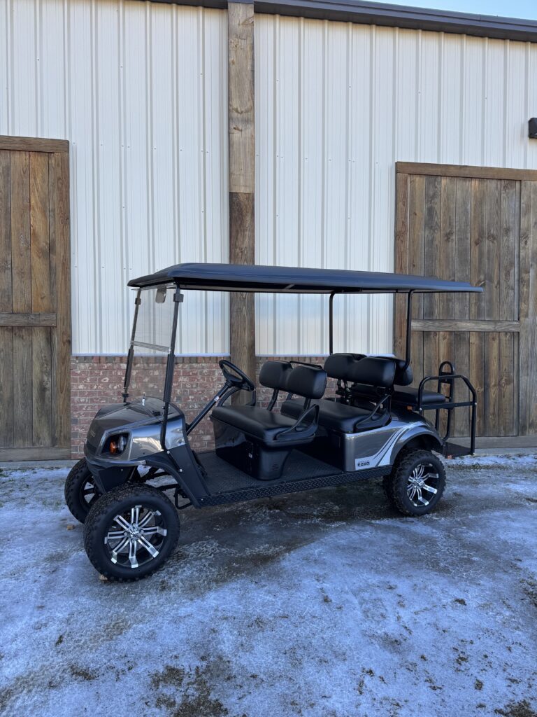 Black golf cart with roof parked on snowy ground outside a building.