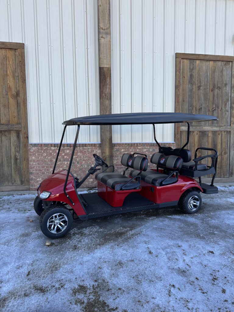 Red six-seater golf cart parked on snowy ground near a building.