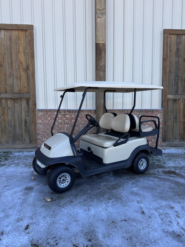 White golf cart parked on a snowy surface near wooden gates.