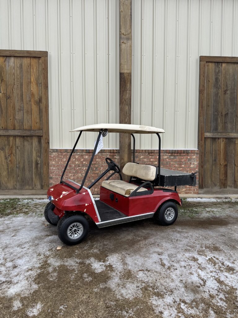 Red golf cart parked outside a building with wooden doors.