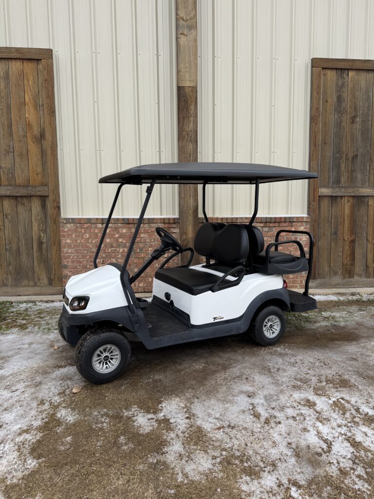White golf cart parked on a snowy driveway beside a wooden fence.