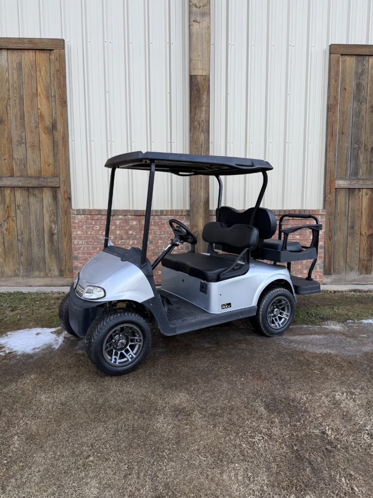 Silver golf cart parked outside a wooden fence.