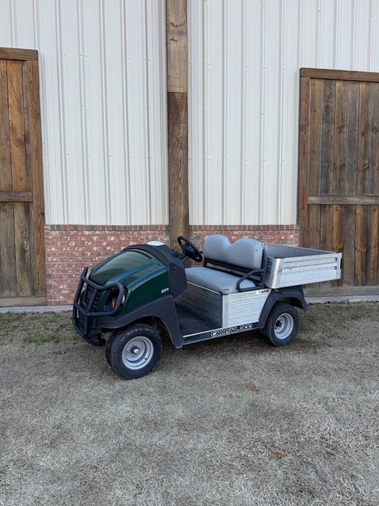 A compact green utility vehicle parked outside wooden doors.