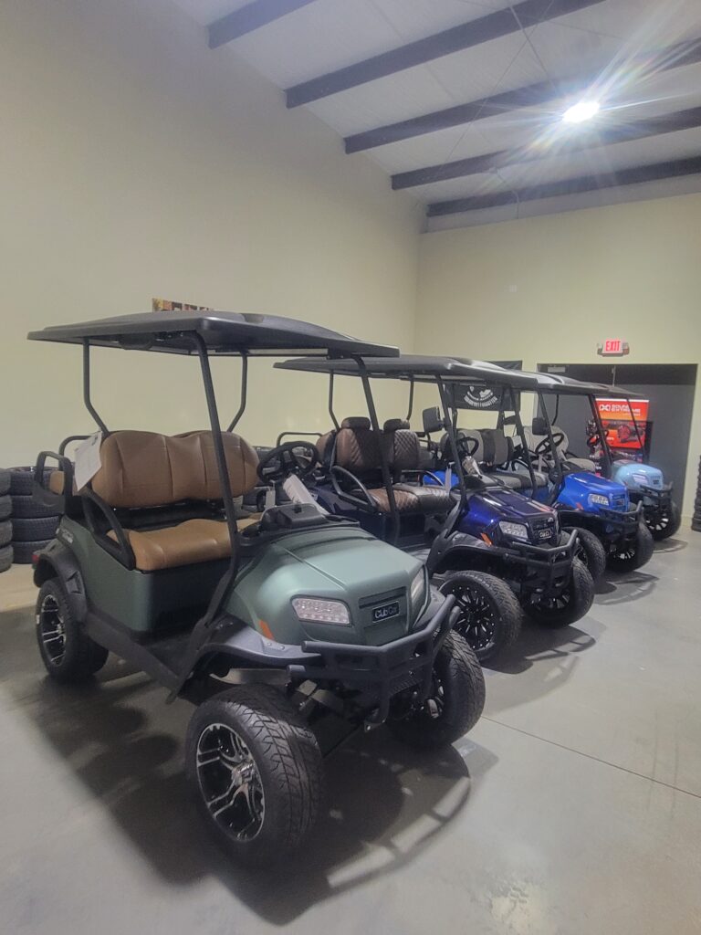 A row of golf carts parked indoors with various colors.