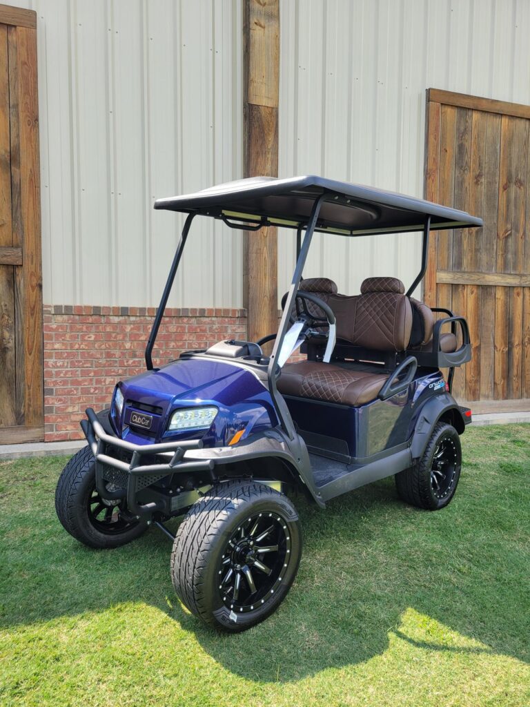 A blue golf cart parked on grass near a wooden fence.