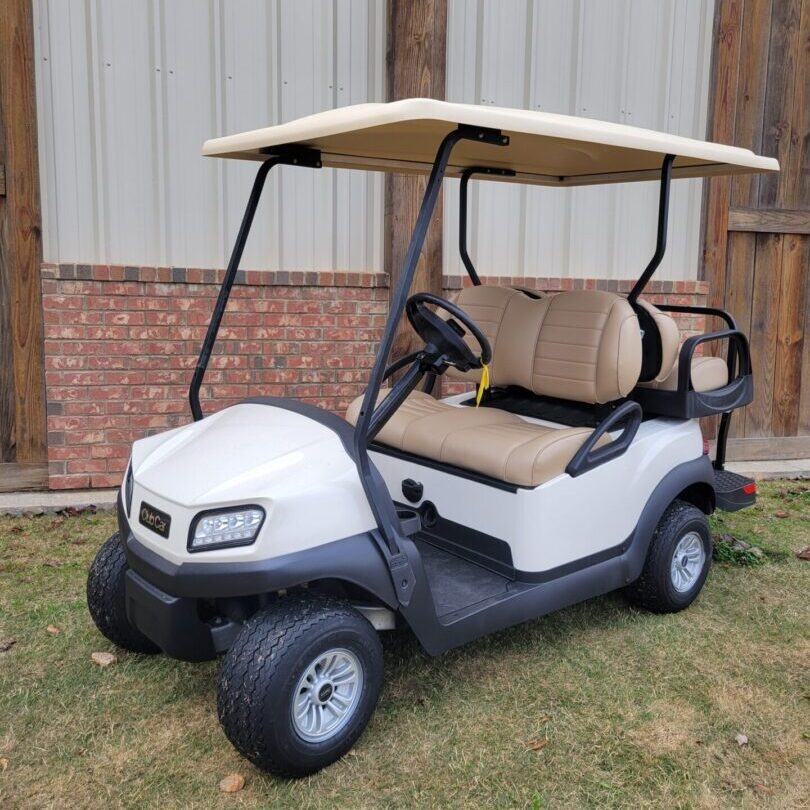 A white golf cart parked on grass near a building.