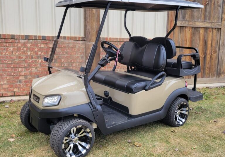 Beige golf cart parked on grass near a brick building.