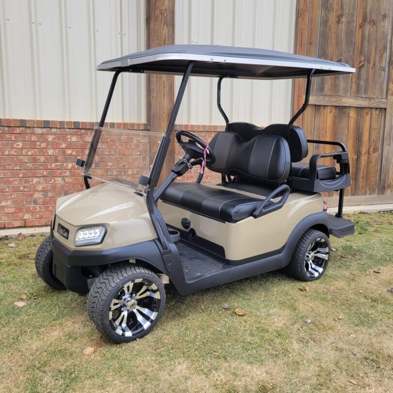 Beige golf cart parked on grass near a brick building.
