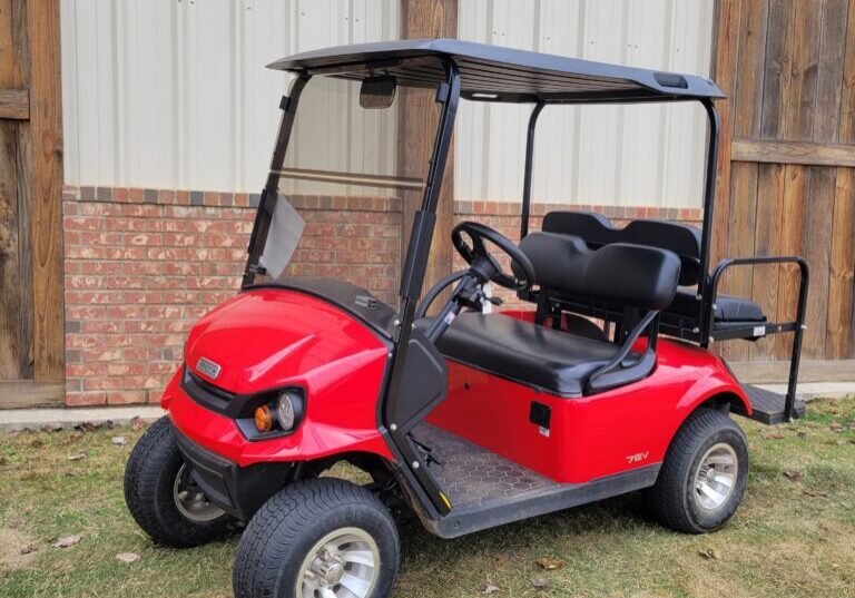 Red golf cart parked on grass near a wooden fence.