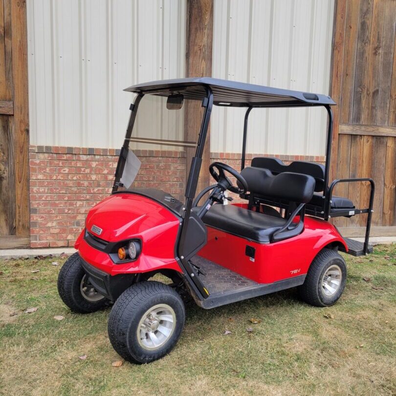 Red golf cart parked on grass near a wooden fence.