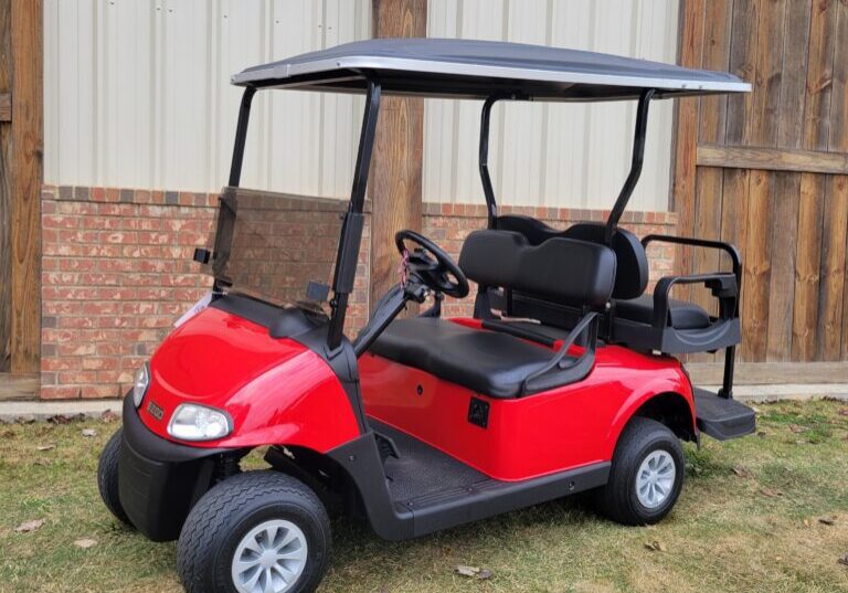Red golf cart parked on grass near a building.