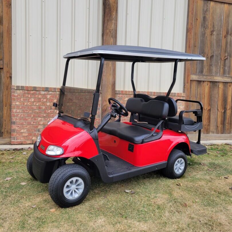 Red golf cart parked on grass near a building.
