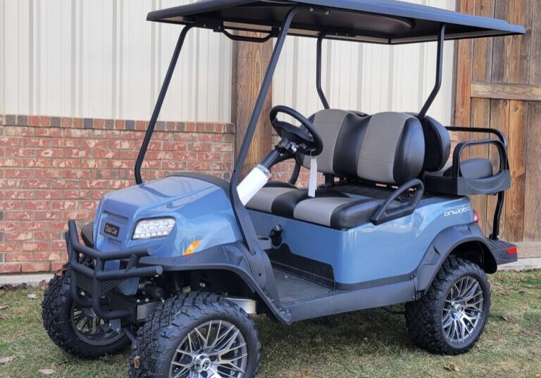 Blue golf cart with lifted suspension and custom wheels parked on grass.