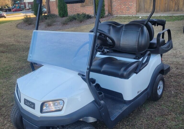 A white golf cart parked on grass with a roof and black seats.