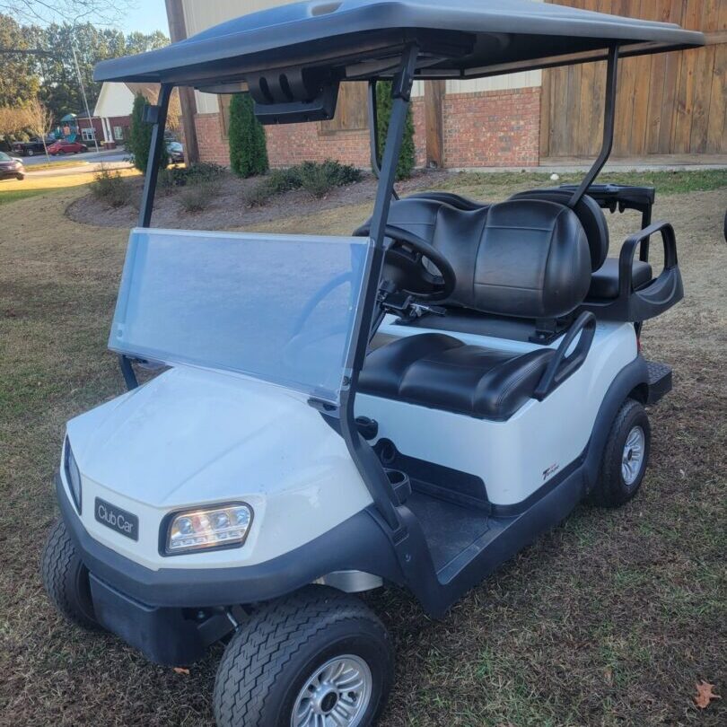 A white golf cart parked on grass with a roof and black seats.