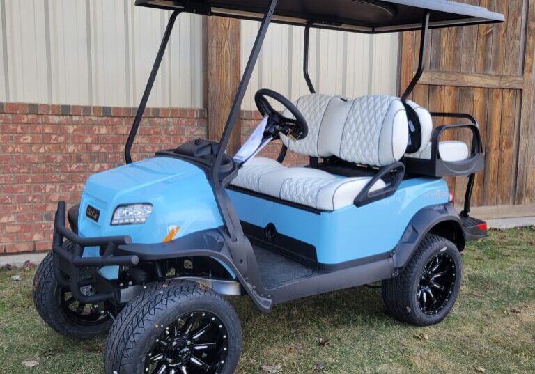 Blue golf cart with black roof and custom wheels parked on grass.