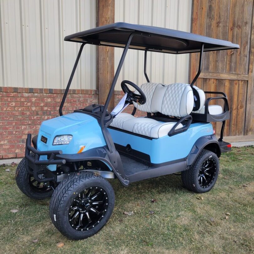 Blue golf cart with black roof and custom wheels parked on grass.