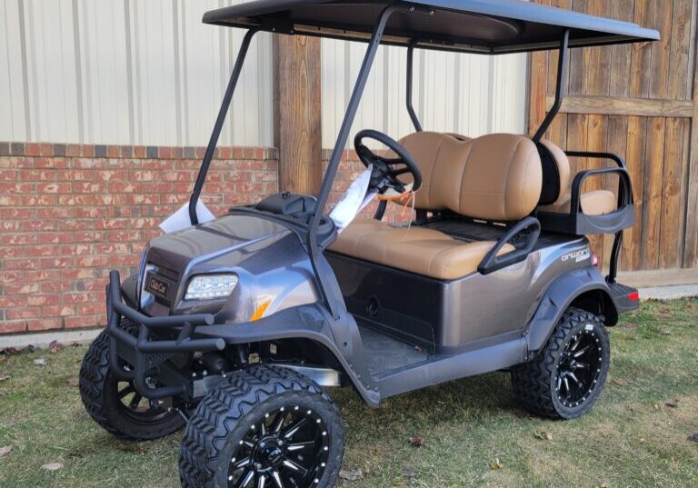 A sleek black golf cart with rugged tires parked on grass.