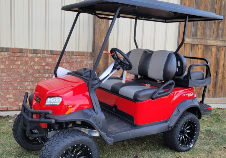 A red lifted golf cart parked on grass near a building.