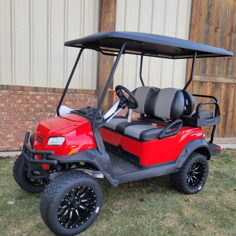 A red lifted golf cart parked on grass near a building.