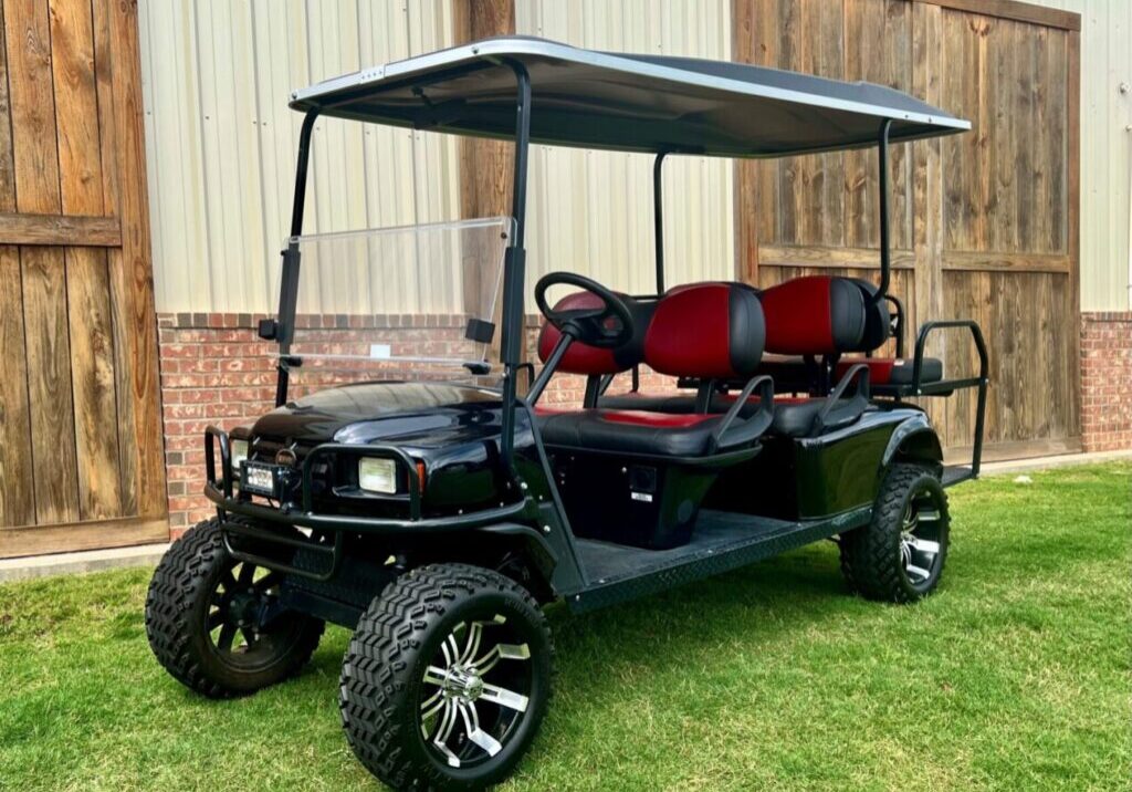 Black six-seater golf cart with red seats parked on grass.