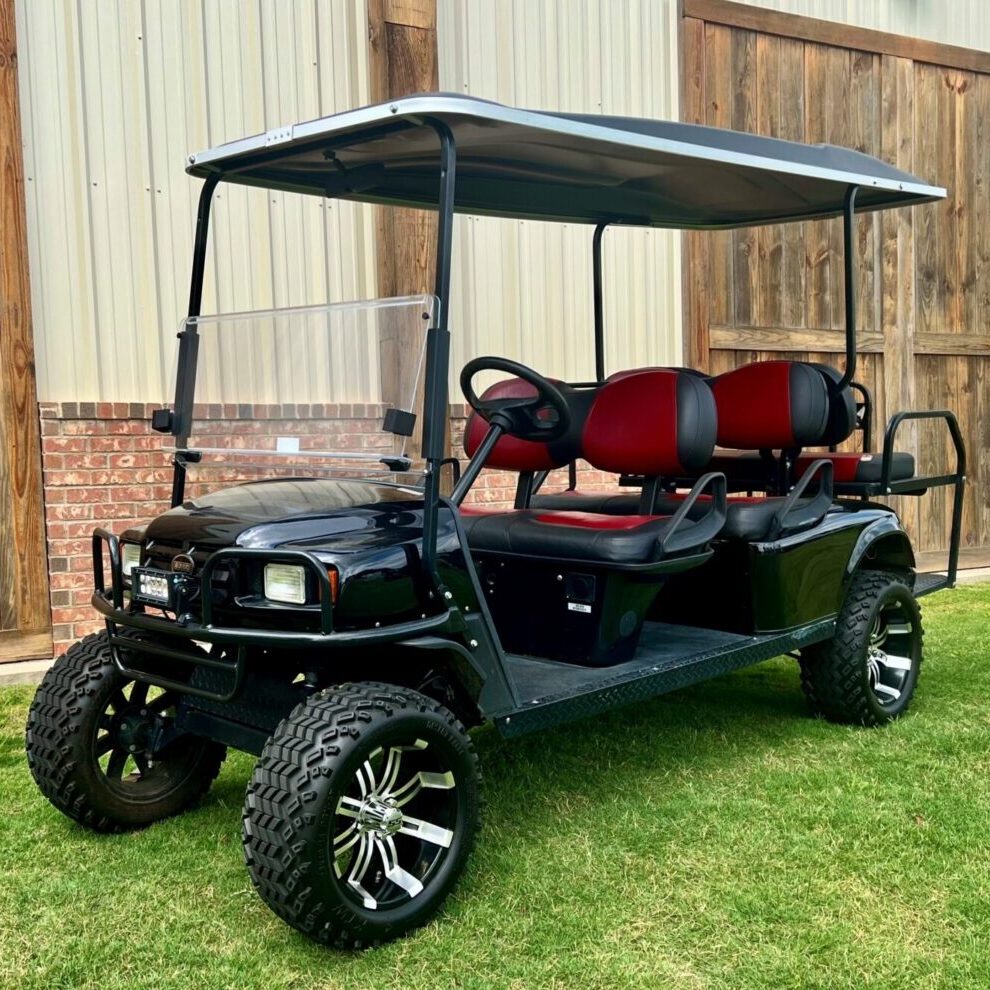 Black six-seater golf cart with red seats parked on grass.