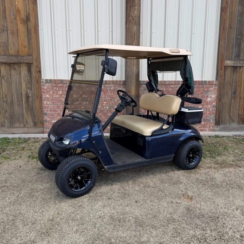 Blue golf cart parked on grass near wooden fence.