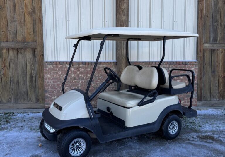 White golf cart parked on a snowy surface near wooden gates.