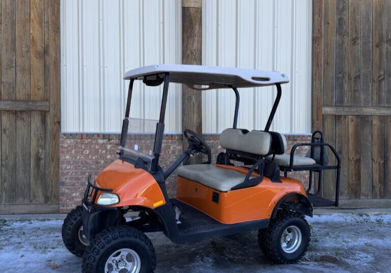 Orange golf cart parked outside near wooden doors.