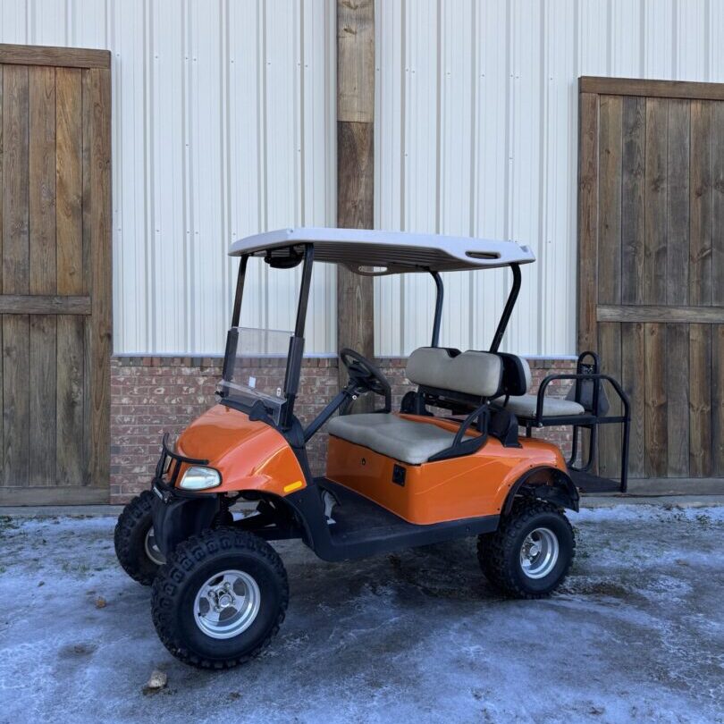 Orange golf cart parked outside near wooden doors.
