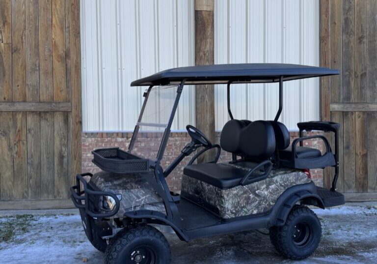 Camouflaged golf cart parked outside a building with wooden doors.