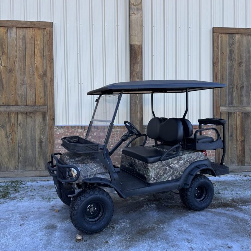 Camouflaged golf cart parked outside a building with wooden doors.