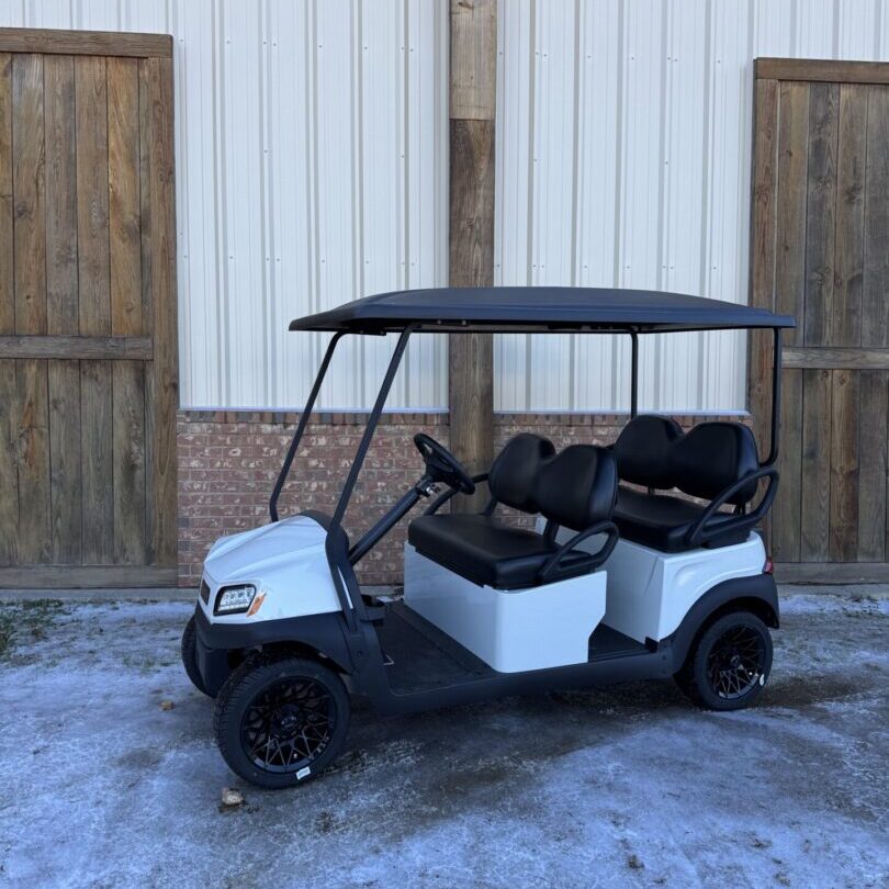 White golf cart with black roof and seats parked outside wooden doors.